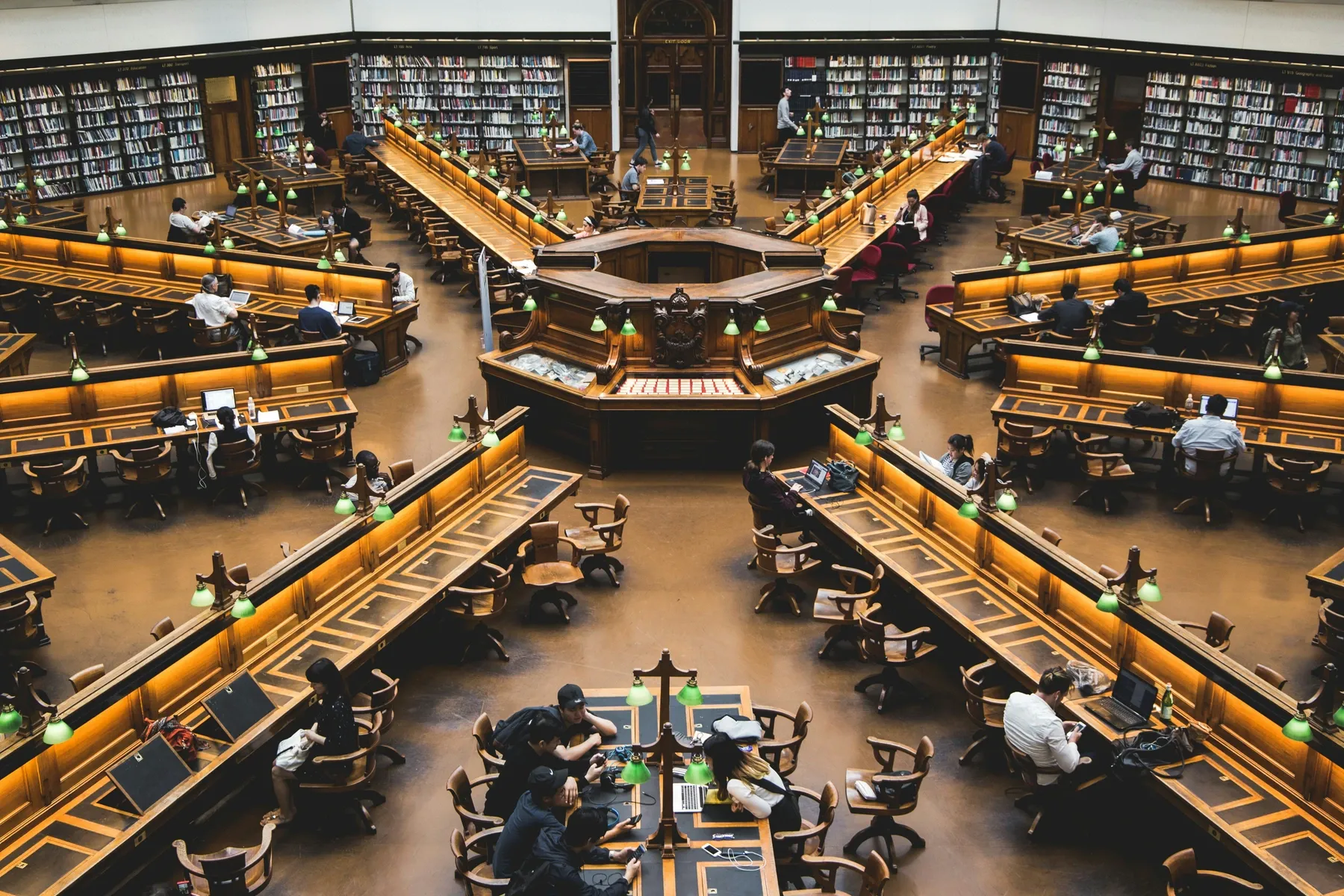 La sala de lectura de una biblioteca vista desde arriba, con personas estudiando en mesas largas.