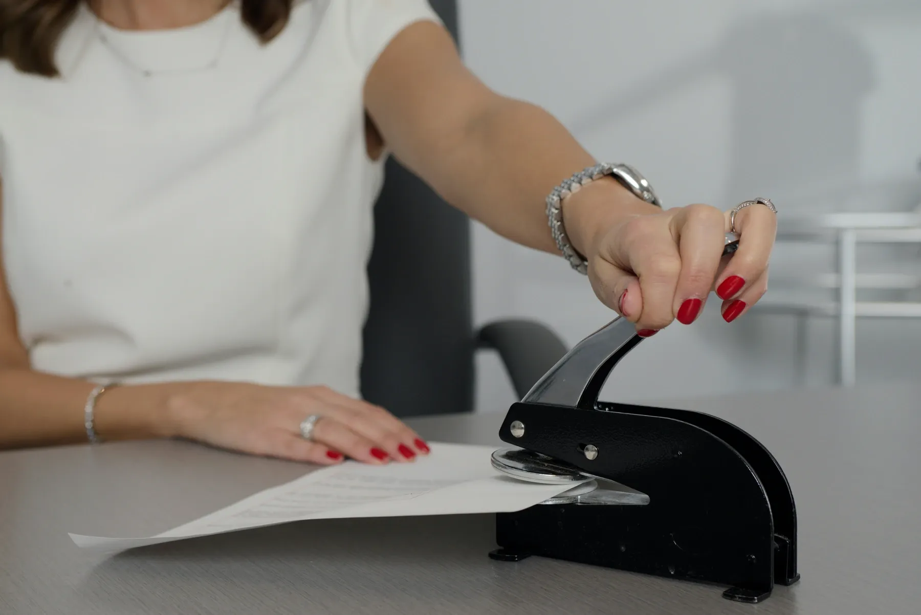 Una mujer sella un documento oficial con un sello de relieve sobre la mesa.
